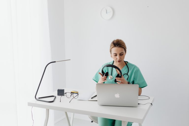 Female doctor sitting at desk with headphones and laptop